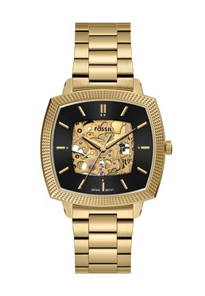Montre Fossil carrée avec un bracelet en acier inoxydable doré, un cadran noir et des mécanismes exposés ornés d'accents dorés et roses.