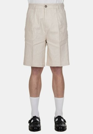 Pantaloncini beige su misura fino al ginocchio con pieghe anteriori, indossati con calzini bianchi e mocassini intrecciati in pelle nera.