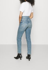 Světle modré džíny s vysokým pasem a úzkým střihem, se sepranými detaily, pěti kapsami a roztrhnutým lemem. Dokončeno černými špičatými botami.