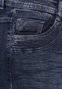 Jean en denim foncé avec une poche avant, des coutures visibles et un léger brillant. Le tissu a une texture lisse avec des variations de couleur subtiles.