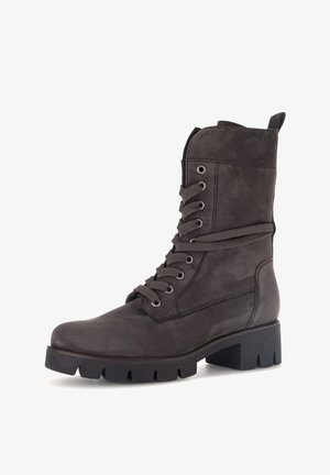 Botte de style combat en cuir marron foncé avec semelle à crampons épaisse, fermeture à lacets sur le devant et languette à l'arrière.