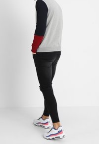 Felpa grigia con maniche blu navy e rosse, abbinata a jeans neri strappati e sneakers bianche con accenti rosa e blu.