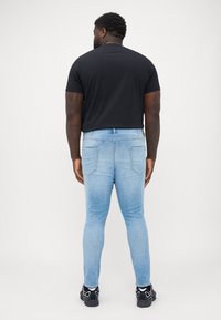 Light blue, skinny jeans with a smooth, slightly distressed texture. Two back pockets and a waistband detail. Black short-sleeve shirt.