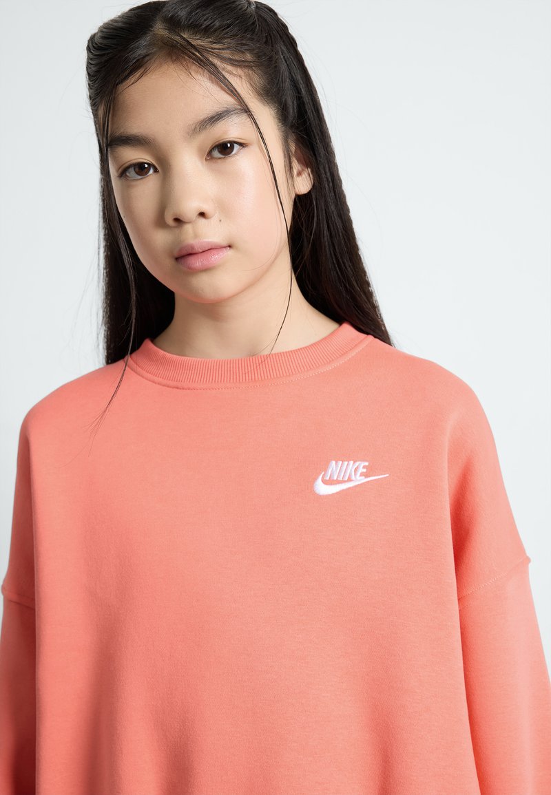 Korallen Nike pulover, oversize kroj, okrogla izrezana ovratnica, mehak tekstur, ima bel logo na levi strani, priložnostna zasnova.