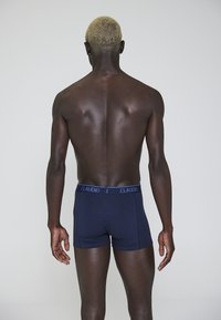 Boxer blu navy con una texture morbida e una cinturina elastica con il logo "CLAUDIO". Indossati da una persona vista di spalle, mostrando la schiena e le braccia.