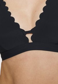 Sutiã preto com bordas onduladas, design em V e um pequeno detalhe em forma de chave no centro. Tecido suave e estilo minimalista.