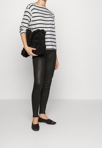 Striped long-sleeve shirt in white and black, black textured woven clutch bag, fitted black leggings, and black flat shoes.
