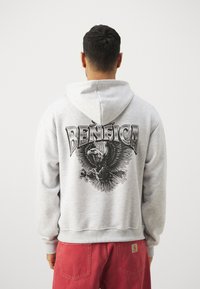 Gray sweatshirt featuring a large black graphic of an eagle and the word "BENFICA" on the back. Hood with textured fabric and ribbed cuffs.