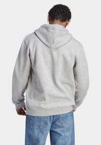 Grå huvtröja med rymlig huva, elastiska muddar och fåll, med vita ränder längs axlarna, tillverkad av ett mjukt bomullsblandat material.