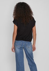 Haut noir oversize avec manches retroussées, associé à un jean denim bleu taille haute comportant cinq poches et une coupe à jambes larges.