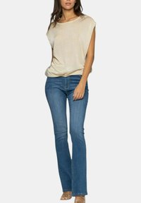 Top beige senza maniche con una vestibilità rilassata, abbinato a jeans blu a zampa d'elefante. Il tessuto è morbido, con una texture liscia e una leggera lucentezza.