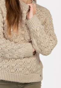 Beige gestrickter Pullover mit massiven Strukturmustern, gerippten Bündchen und Saum. Das Material wirkt weich mit dezenten Schimmerakzenten.