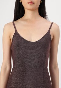 Robe à bretelles spaghetti en métal brun avec un décolleté en V profond, un tissu texturé et une silhouette ajustée, mettant en valeur des détails de légère brillance.