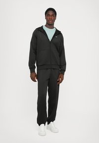 Svart zip-up hoodie med sidofickor, tillsammans med svarta byxor. Har en ljusblå undertröja och vita sneakers. En enkel, atletisk design.