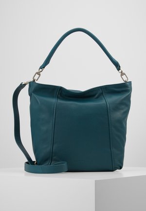 Sac à main en cuir bleu sarcelle avec une poignée courte et une longue bandoulière amovible, présenté sur une surface blanche avec un fond neutre.