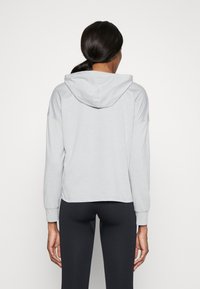 Harmaa huppari, joka on rentoa mallia, varustettuna nyöritettävällä hupulla, pitkillä hihoilla ja ribatulla resorilla. Pehmeä puuvillasekoitekangas. Korkeat tummat legginsit.