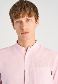 Lichtroze overhemd met knopen, een mandarijnkraag, zachte textuur, een borstzak en een klein logolabel aan de zijkant.