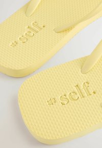 Gele flip-flops gemaakt van geborsteld rubber, met een logo in reliëf op de voetbed en bijpassende banden met een gladde afwerking.