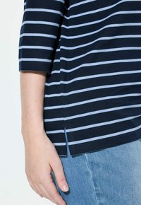 Laivansinisestä raidallisesta t-paidasta, jossa on vaaleansinisiä vaakaraitoja, lyhyet hihat ja sivuaukot. Yhdistetty vaaleansinisiin farkkuihin.