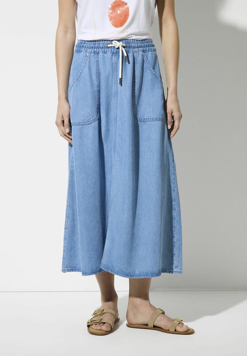 Lichtblauwe dennen rok met een elastische tailleband, verstelbaar trekkoord en twee voorzakken. A-lijnvorm, vloerlang ontwerp.
