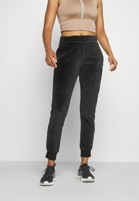 Svarta velourjoggingbyxor med elastisk midja, smalnande manschetter och sidodetaljer. I kombination med en beige crop top och svarta sneakers.