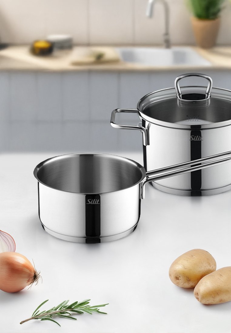 Garnek ze stali nierdzewnej, jeden z przezroczystą pokrywką, o polerowanym wykończeniu. W pobliżu znajdują się szalotki, ziemniaki i gałązka rozmarynu.