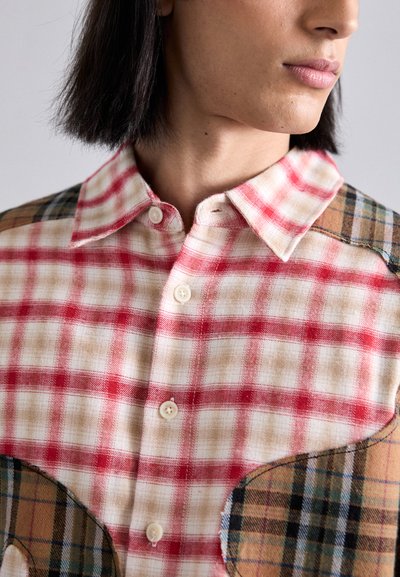 Button-up shirt featuring a red and beige plaid pattern with a tan shoulder patch in a check design. Soft fabric texture, short collar.
