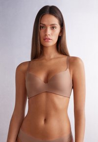 Soutien-gorge moulé marron avec des bretelles fines et ajustables et une texture lisse. Présente un décolleté en V et un matériel minimal pour un look sans couture.