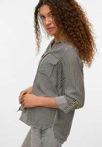 Bluse med sort-hvide striber i et let materiale, krave, brystlomme og opsmøgede ærmer, der holdes på plads med knapper.