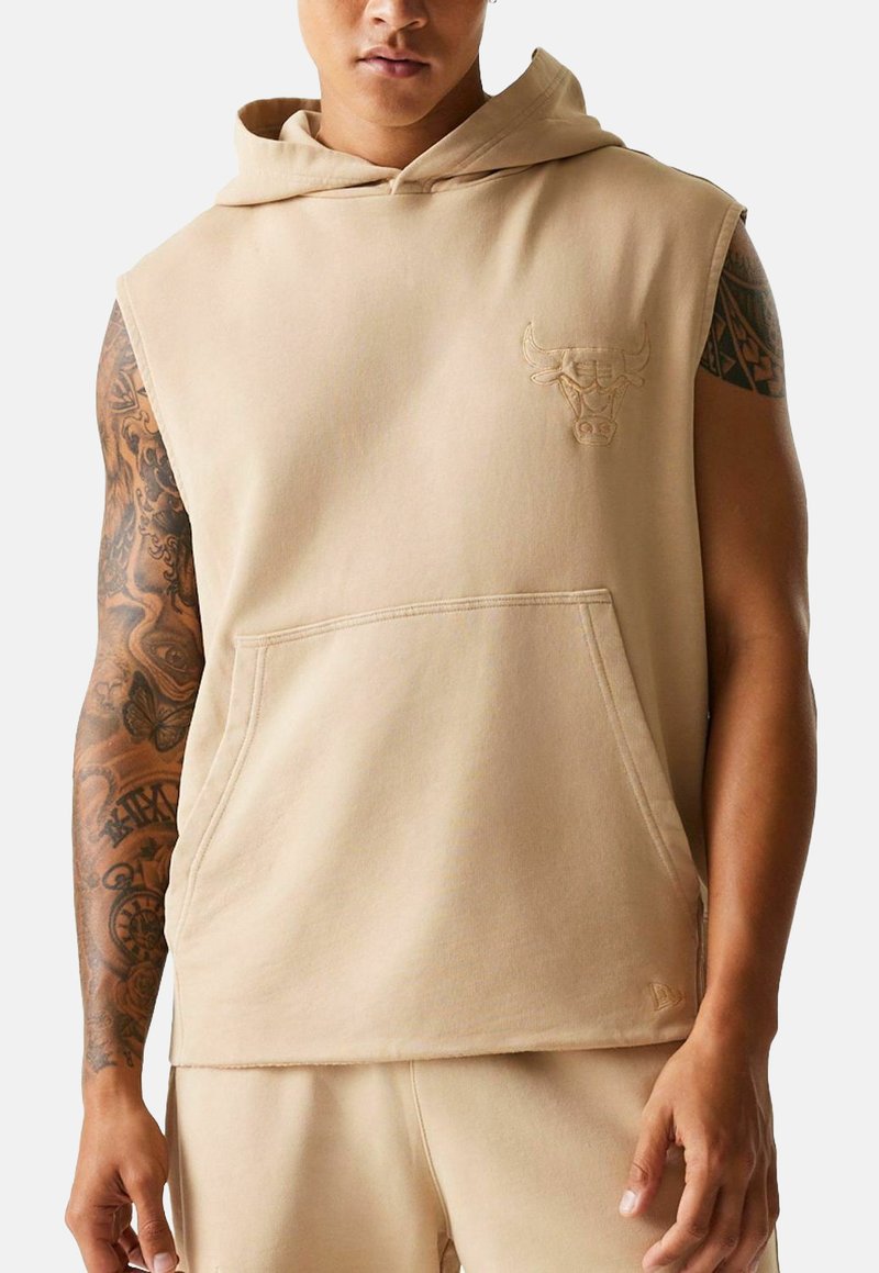 Beige ärmelloses Kapuzenshirt aus weichem Stoff, mit einer Fronttasche und einem reliefierten Stierlogo auf der Brust. Glatte Textur.