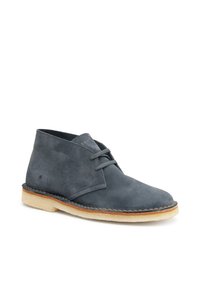 Stivaletti in suede grigi con punta arrotondata, due chiusure a lacci e una suola in gomma di colore chiaro. Presentano un delicato dettaglio di cucitura.