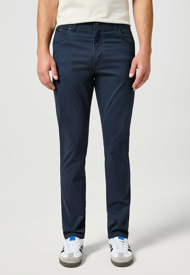 Pantalones azul marino hechos de una mezcla de algodón, con bolsillos estructurados y un diseño de pierna recta, combinados con zapatillas blancas informales.