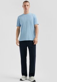 Jasnoniebieska koszulka z okrągłym dekoltem połączona z granatowymi spodniami casualowymi. Model ma na sobie białe buty sportowe. Prosty krój z krótkimi rękawami.