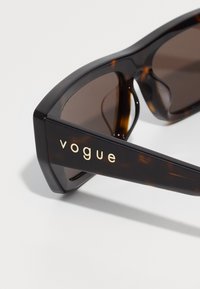 Gafas de sol rectangulares de carey oscuro con lentes marrones, que presentan el logo "Vogue" en oro en la patilla.
