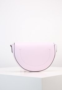 Růžová kožená kabelka s polosférickým tvarem, zdobená černým šitím a s klopovým uzávěrem. Hladký povrch a minimalistický design.