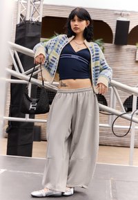 Grauweite Sweatpants, blaue und cremefarbene gemusterte Strickjacke, schwarze Tasche mit Hardware-Details und silberne Ballerinas. Minimale Accessoires.