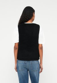 Black fleece vest with a textured surface, sleeveless design, and rounded neckline, paired with blue high-waisted jeans.