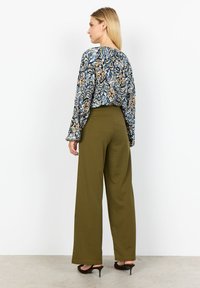 Blusa a fiori nei toni del blu, beige e nero, abbinata a pantaloni a gamba larga color verde oliva con vita alta, indossati con tacchi a spillo marroni.