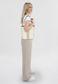 Canvas tote bag in crème met zwarte rand en drie verticale strepen. Heeft een gestructureerde vorm en lange schouderriem voor gemakkelijk dragen.