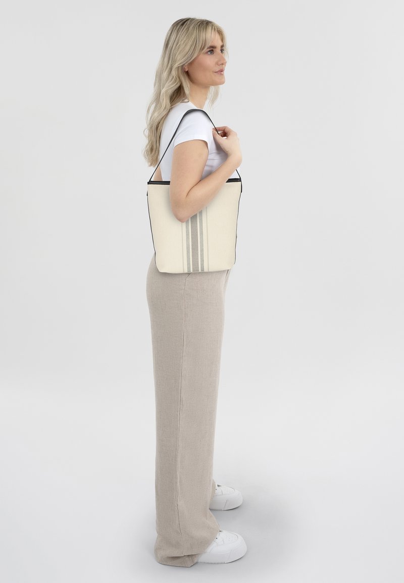 Canvas tote bag in crème met zwarte rand en drie verticale strepen. Heeft een gestructureerde vorm en lange schouderriem voor gemakkelijk dragen.