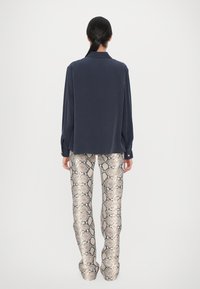 Camisa de manga larga azul marino con cuello, combinada con pantalones de estampado de serpiente en un tono beige claro que presentan una superficie brillante y texturada, y un corte ajustado.