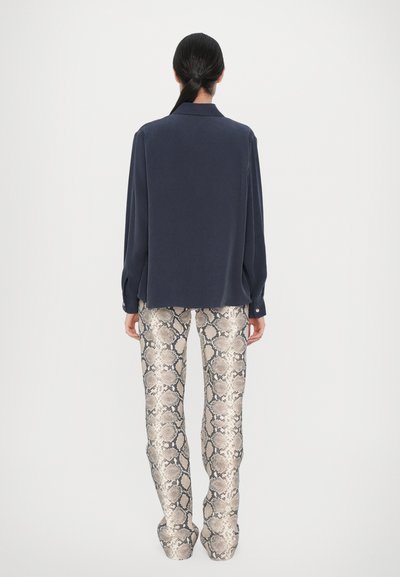 Cămașă lungă, de culoare bleumarin, cu guler, asortată cu pantaloni din stofă bej deschis, cu imprimeu de șarpe, având o suprafață lucioasă și texturată, cu croială conică.