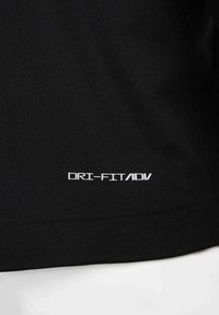 Maglietta sportiva nera realizzata in tessuto traspirante, con una texture liscia e il marchio bianco "DRI-FIT ADV" sul bordo inferiore.