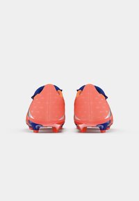 Las botas de fútbol de color coral brillante presentan un empeine liso, un diseño texturizado con patrones triangulares y acentos azules en el collar y la suela.