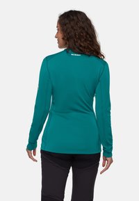 Türkisfarbenes Langarmshirt mit hohem Kragen, glatter Textur und dezentem Logodetail auf der Rückseite. Entwickelt für Activewear, figurbetonte Silhouette.