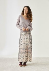Suéter gris claro con escote en V, combinado con una falda larga con estampado floral en beige, azul marino y colores pastel. Zapatos oscuros completan el conjunto.