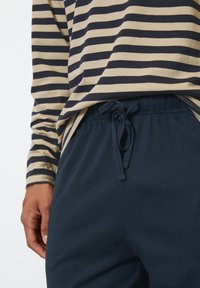 Marineblaue Jogginghosen mit elastischem Bund und Kordelzug, kombiniert mit einem gestreiften Langarmshirt in Beige und Marineblau. Weicher, lässiger Stoff.