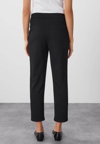 Svarta byxor i stretchigt material med elastisk midja, som har två bakfickor, tapered bendesign och en jämn textur.