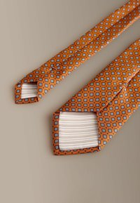Narancssárga nyakkendő kék és fehér mintás geometriai mintával. A végek ellentétes, csíkos anyagból készültek. Szatén textúra.