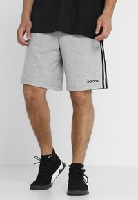 Grå träningsshorts i bomullsblandning med svarta sidostråkar och en broderad logotyp. Bärs med svarta sneakers och en svart tröja.